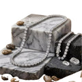 a necklace with a large, sparkling diamond pendant, resting on a marble surface. The necklace is surrounded by various natural elements, including rocks and crystals, creating a visually striking and elegant display.