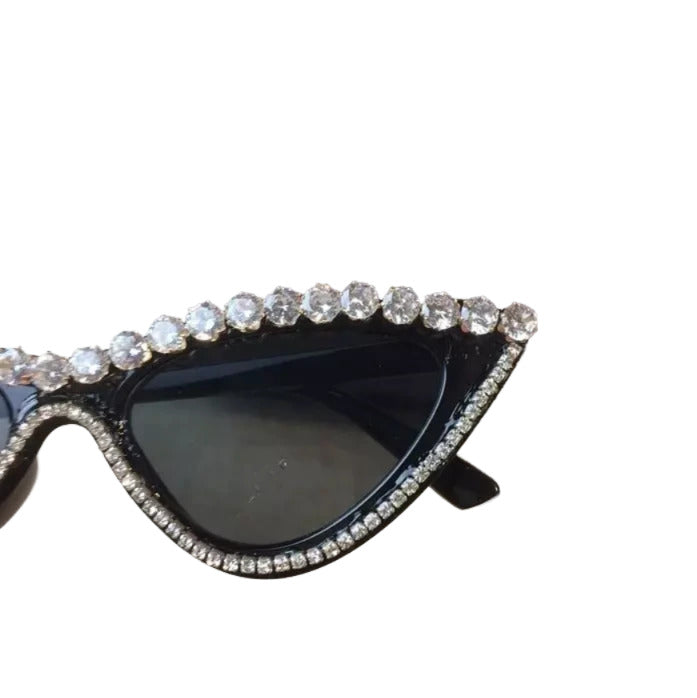 A pair of black sunglasses with a sparkling rhinestone frame, placed on a surface with a blurred background.